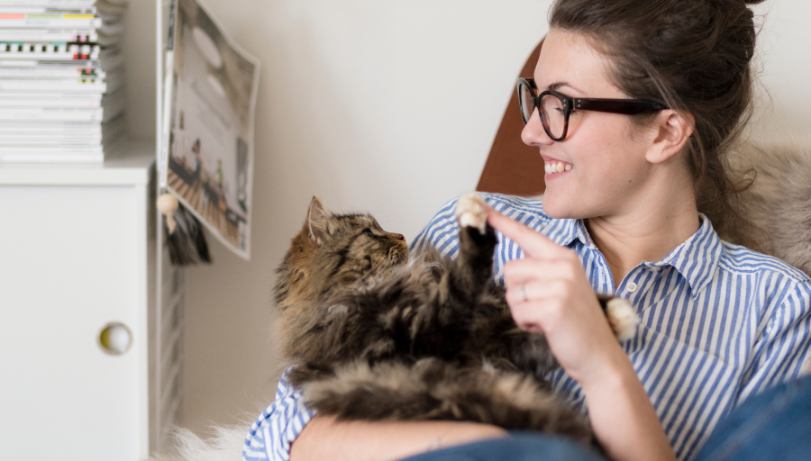 Γυναίκα κάθεται με τη γάτα της στην αγκαλιά της αγγίζοντας την πατούσα της με το δάχτυλό της